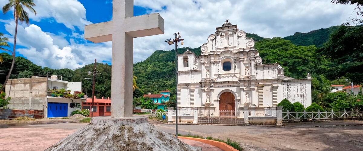 A large white cross, a historic church, and a mountainous landscape.