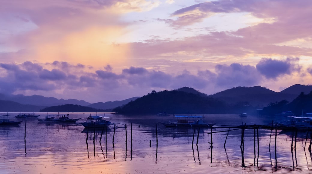 Pretty Pink orange Sky cloudscape over an island with reflection and wooden traditional filipino boats at Sunset on the Island of Coron