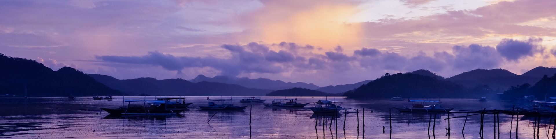 Pretty Pink orange Sky cloudscape over an island with reflection and wooden traditional filipino boats at Sunset on the Island of Coron