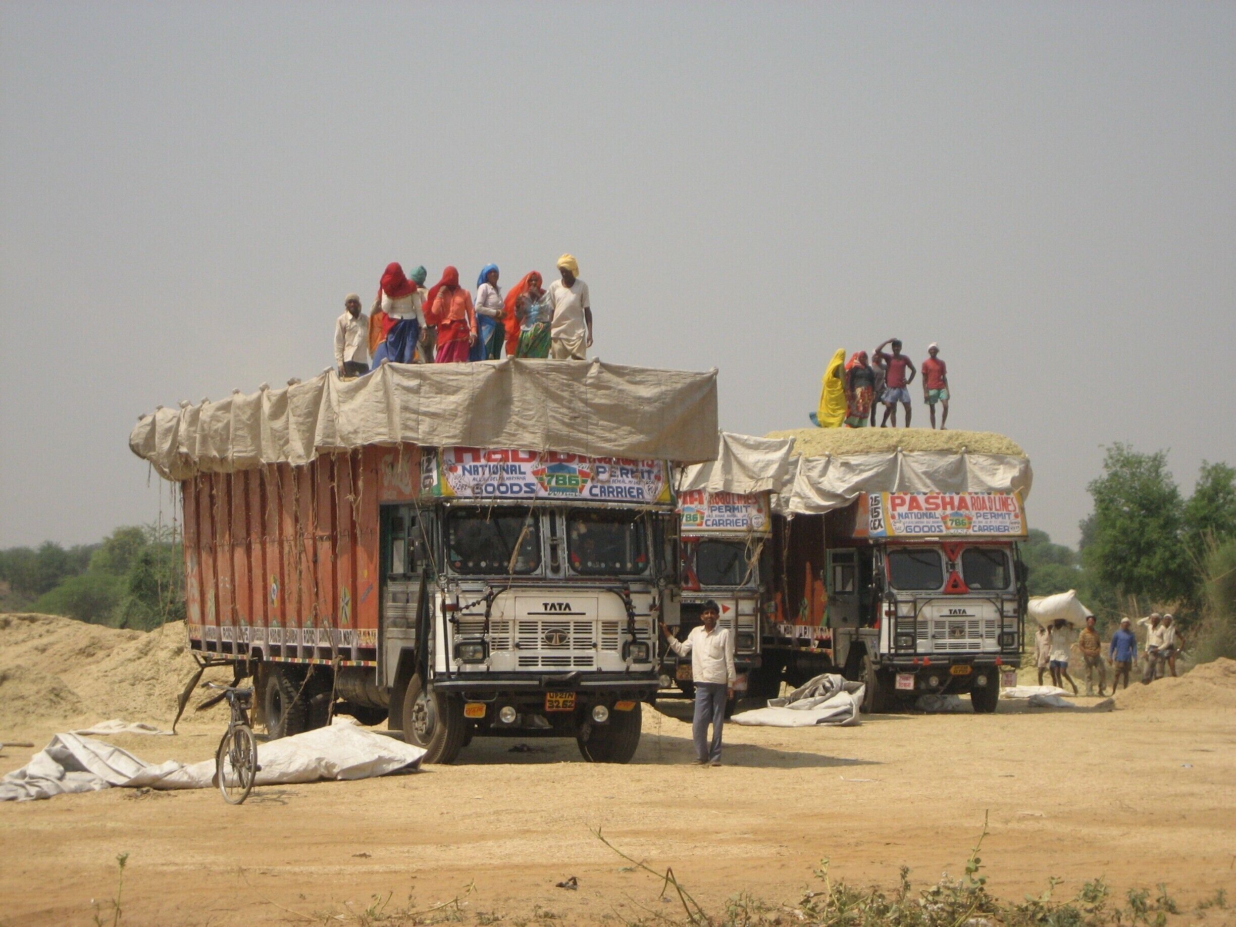 Two trucks with people standing on top, surrounded by sandbags and a barren landscape.