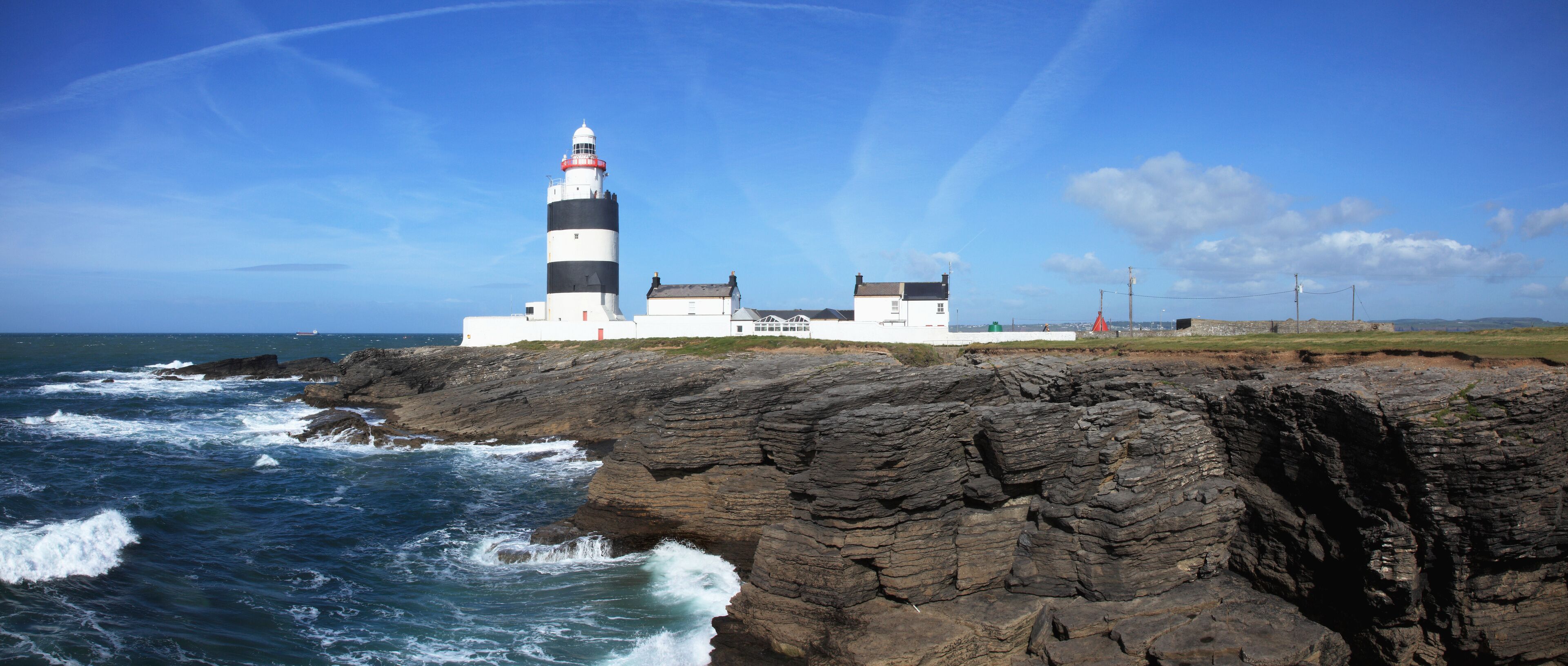 A lighthouse on a rocky coastline with waves crashing against it.
