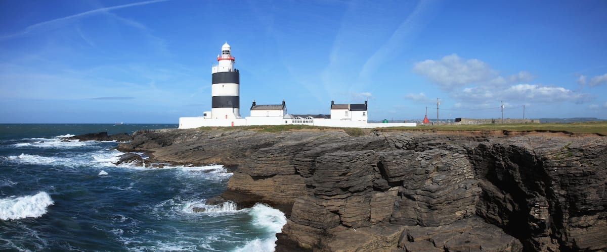 A lighthouse on a rocky coastline with waves crashing against it.