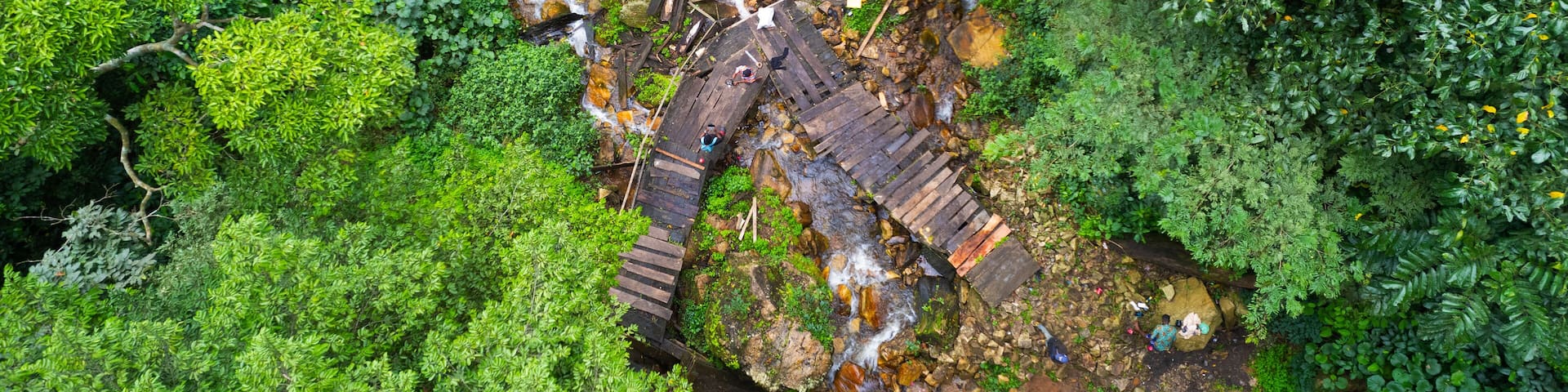 Aerial view of a rustic wooden structure nestled amidst a vibrant green forest, with a small stream flowing beneath, creating a tranquil escape, Ado Ekiti, Ekiti, Nigeria.