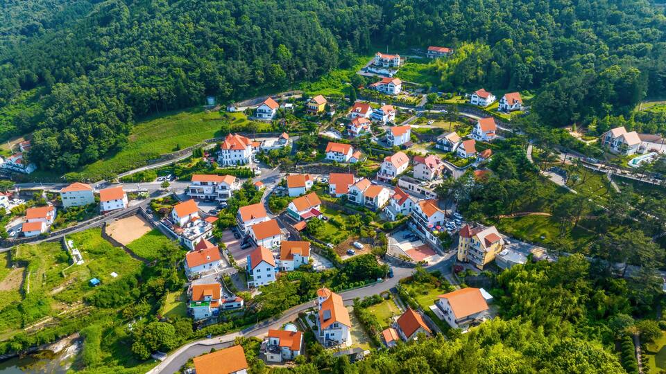 A densely packed village with red-roofed houses nestled in a lush valley surrounded by forested hills.