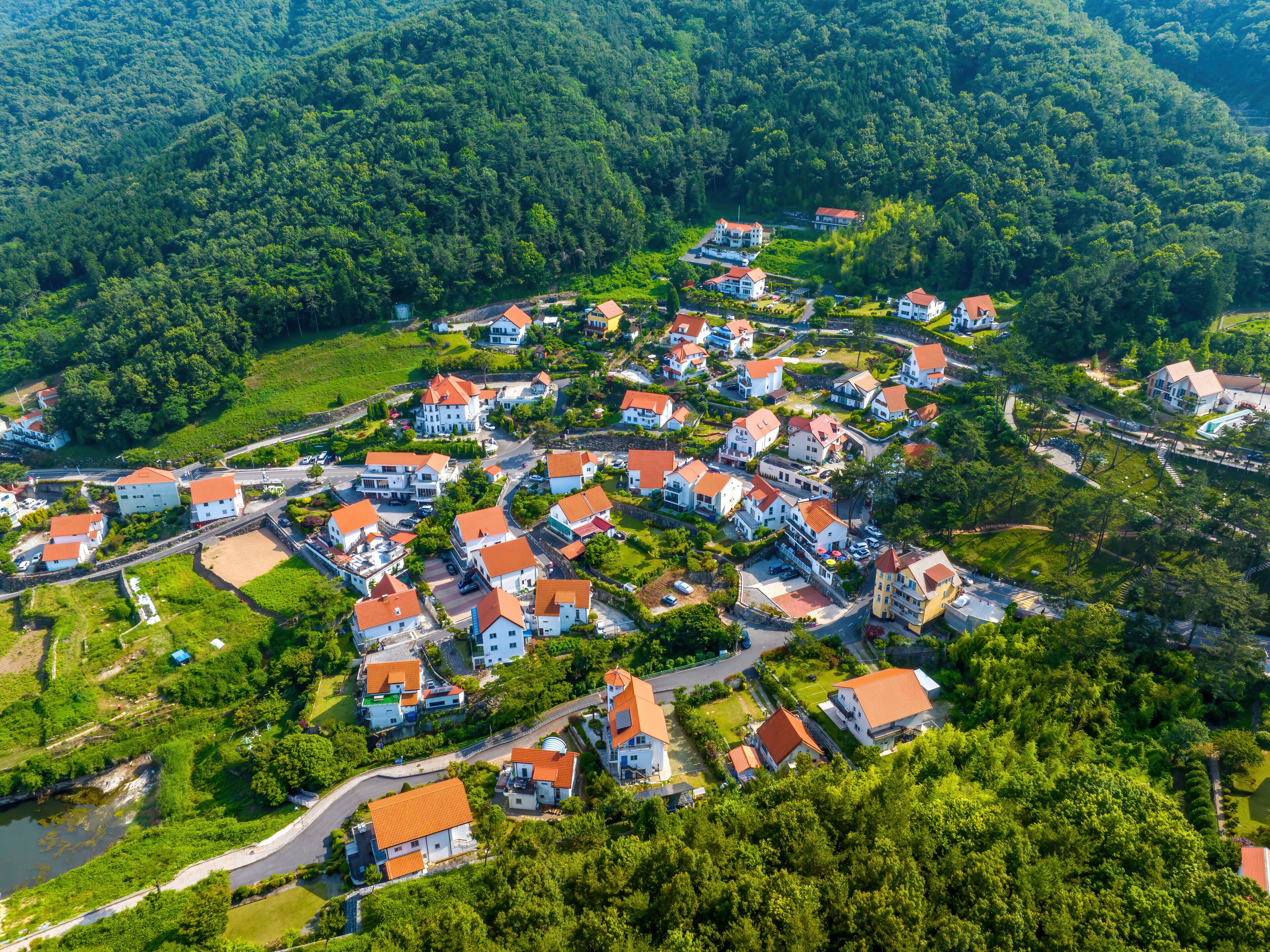 A densely packed village with red-roofed houses nestled in a lush valley surrounded by forested hills.
