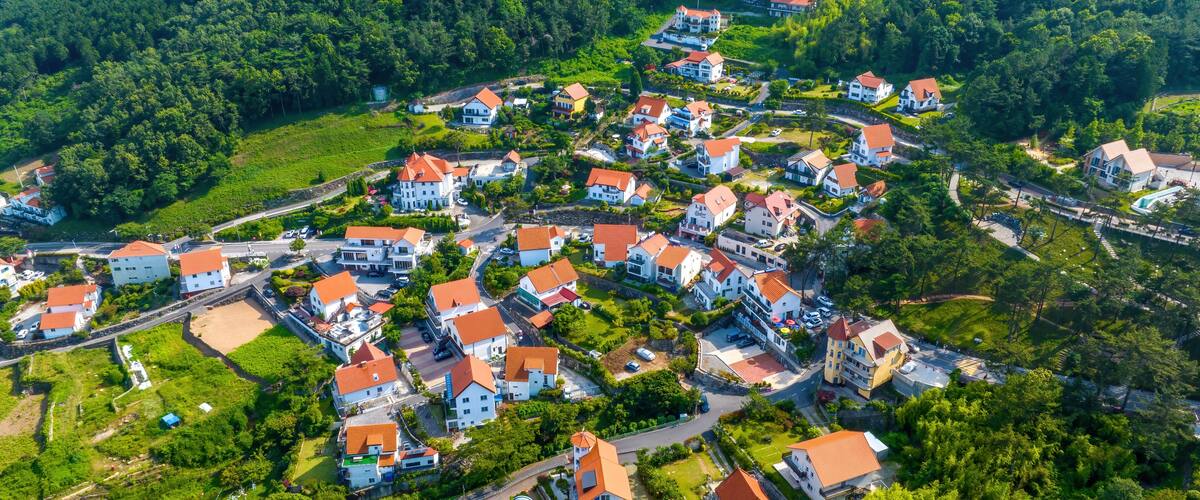 A densely packed village with red-roofed houses nestled in a lush valley surrounded by forested hills.