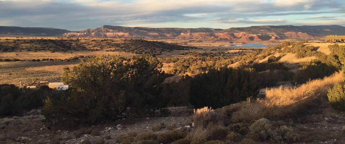 A vast landscape with rolling hills, sparse vegetation, and a distant body of water under a partly cloudy sky.
