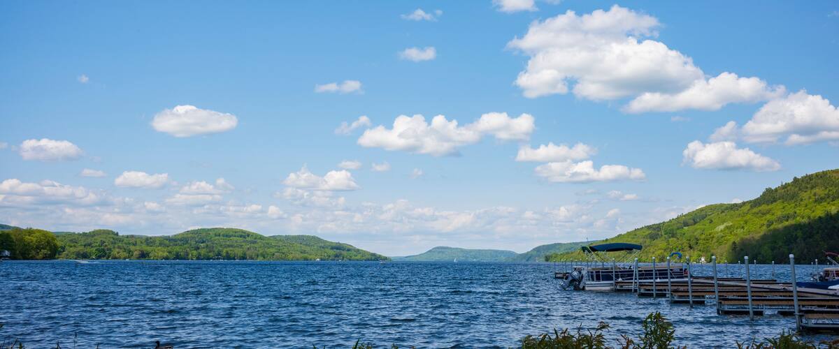 A calm lake with wooden docks, surrounded by green hills and a clear blue sky.