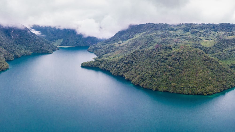 Aerial view of the Laguna Brava in Guatemala, on a cloudy day where you can see its turquoise water and the beautiful mountains that surround the lake.