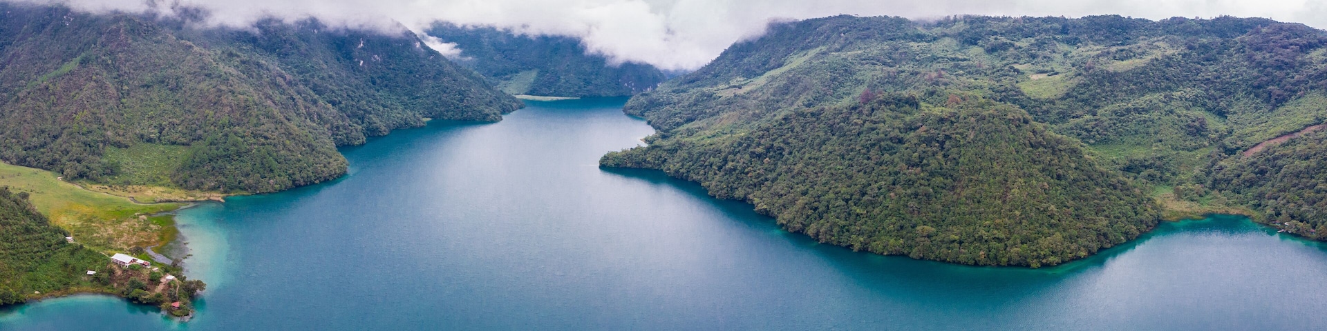 Aerial view of the Laguna Brava in Guatemala, on a cloudy day where you can see its turquoise water and the beautiful mountains that surround the lake.