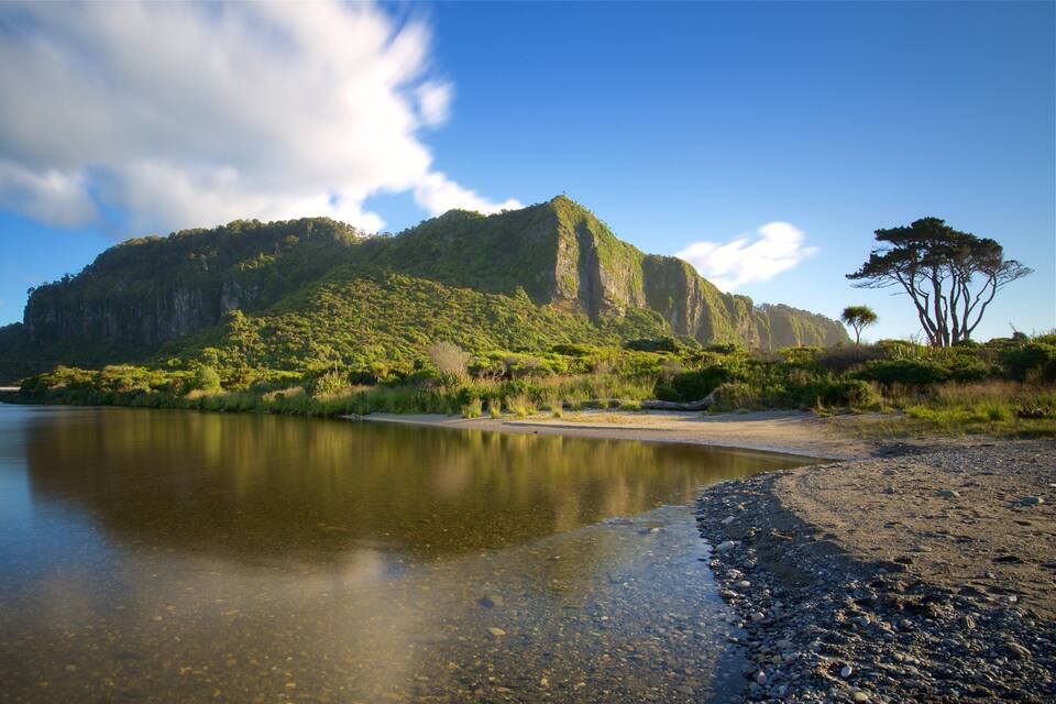A calm river with a rocky shoreline, a bridge, and a forested mountain in the background.
