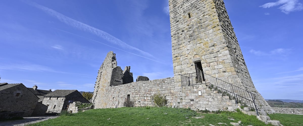 A stone tower with battlements, surrounded by ruins and a clear blue sky.