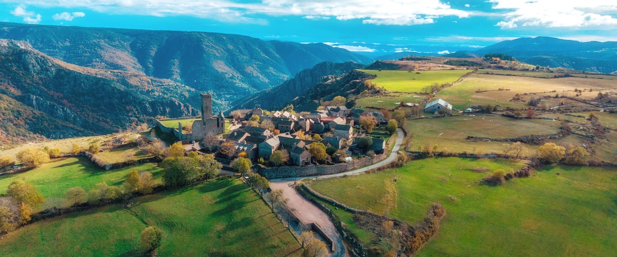 Ein Dorf mit einer markanten Kirche, umgeben von grünen Feldern und Bergen im Hintergrund.