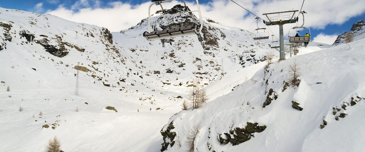 A snowy mountain with ski lifts and rocky terrain.