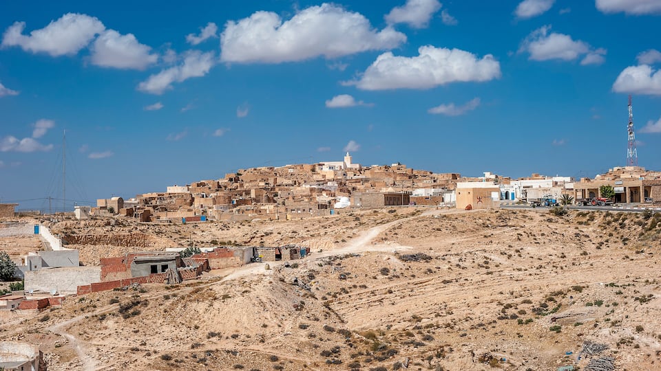 A hilly town with buildings, a mosque, and a communication tower.