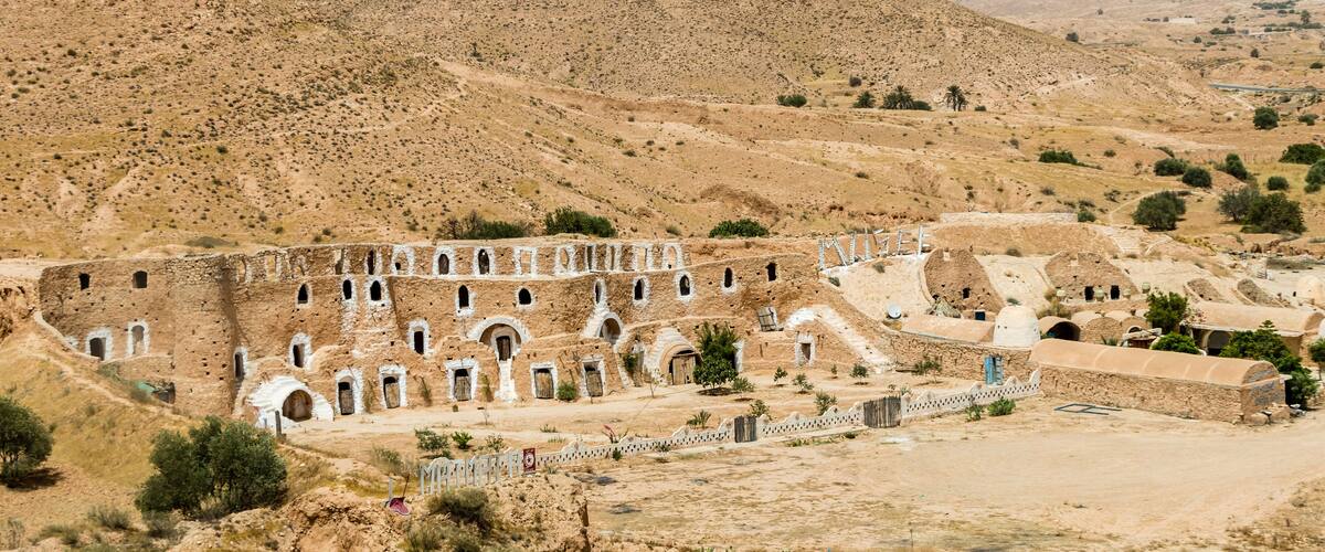 A historical site with ancient architecture, including a large building with multiple arched doorways and a fortress-like structure.