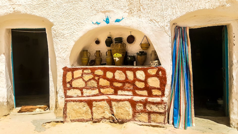 A rustic stone wall with pottery and a striped curtain.