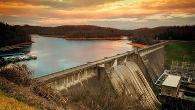 A dam with a lock system, a calm river, and a forested landscape during sunset.
