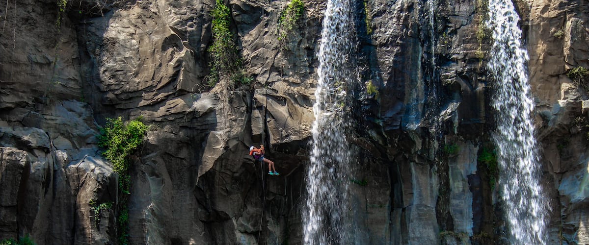 A person rappelling down a cliff with waterfalls in the background.