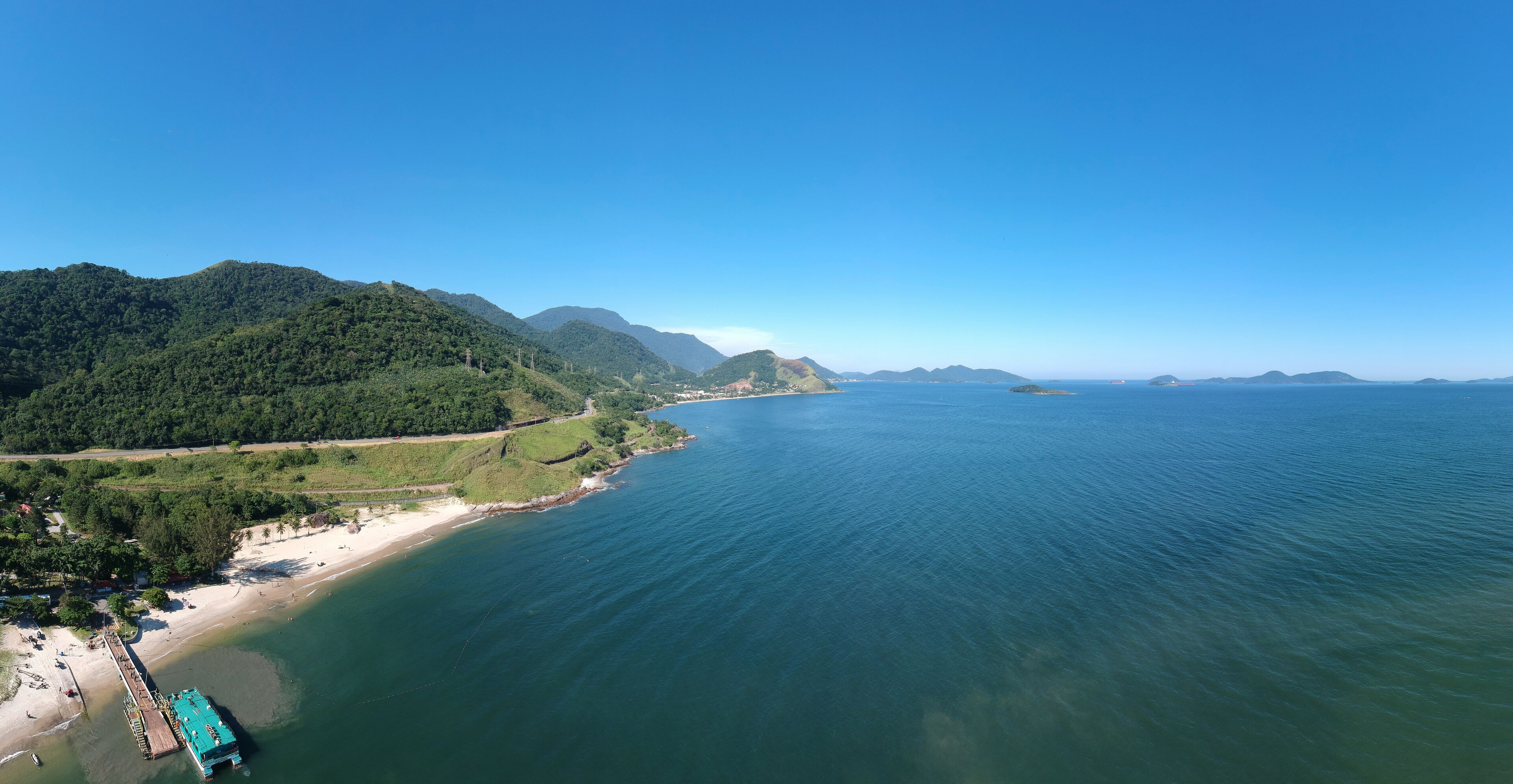 A coastal landscape with a beach, a pier, and a mountainous backdrop.