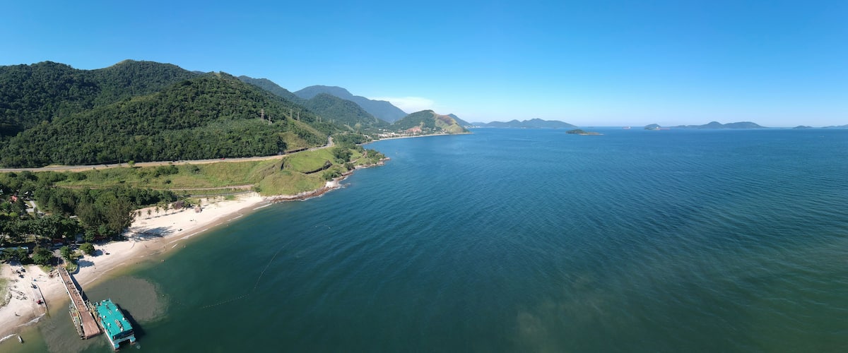 A coastal landscape with a beach, a pier, and a mountainous backdrop.
