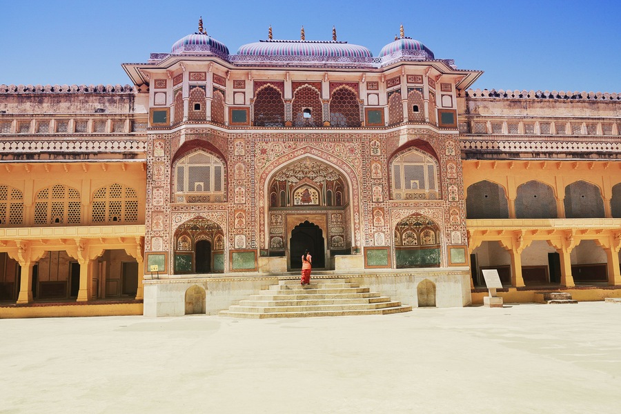 Woman tourist at Ganesh Pol gateway decorated entrance to Amber Palace or Maharaja's residence in Amer Fort Jaipur Rajasthan India.