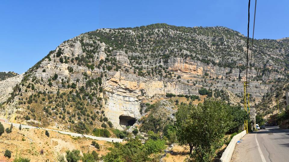 A mountainous landscape with a road, a tunnel, and a building on the right.
