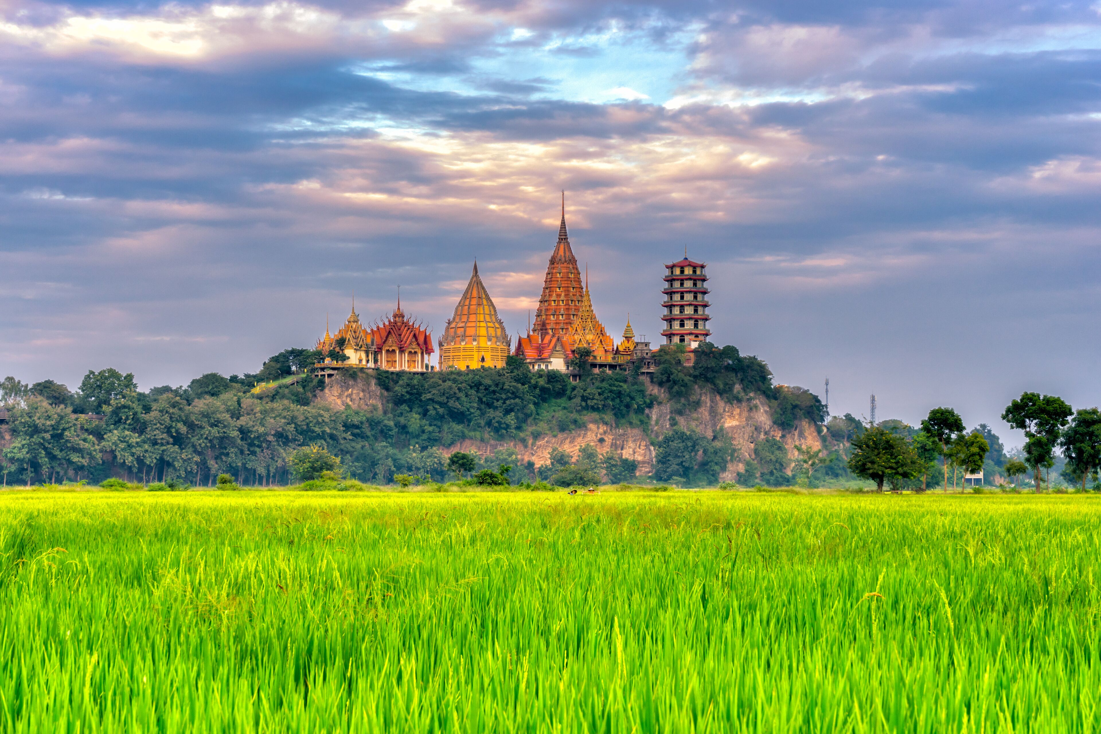 Sunset scence of Wat Tham Sua Temple with rice fields in Kanchanaburi Province, Thailand.