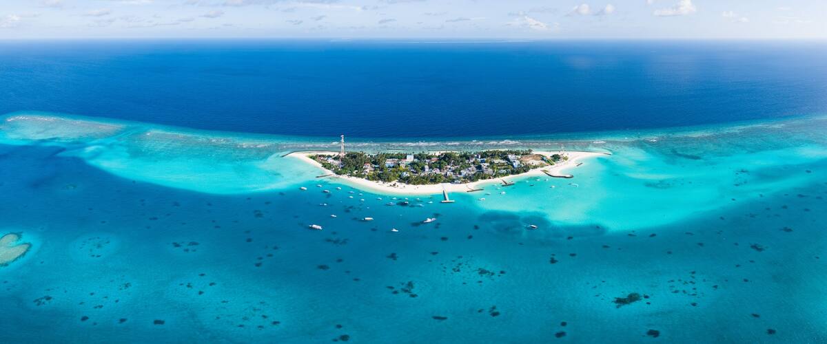 An aerial view of a turquoise island with clear waters, surrounded by smaller islets and a lighthouse.