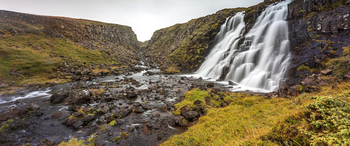 A waterfall cascading down a rocky hillside into a river.