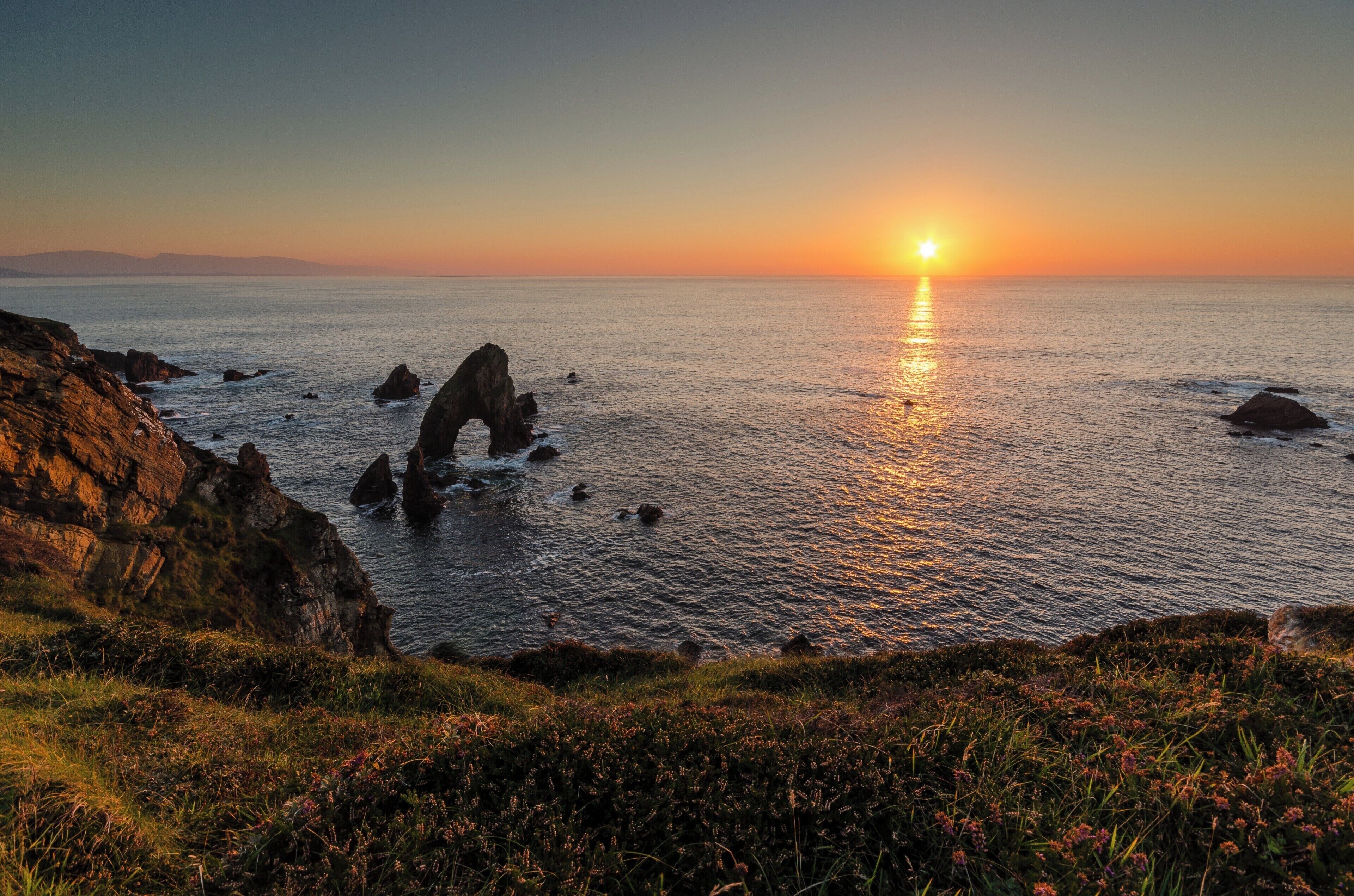 A coastal sunset with rocky formations and calm sea.