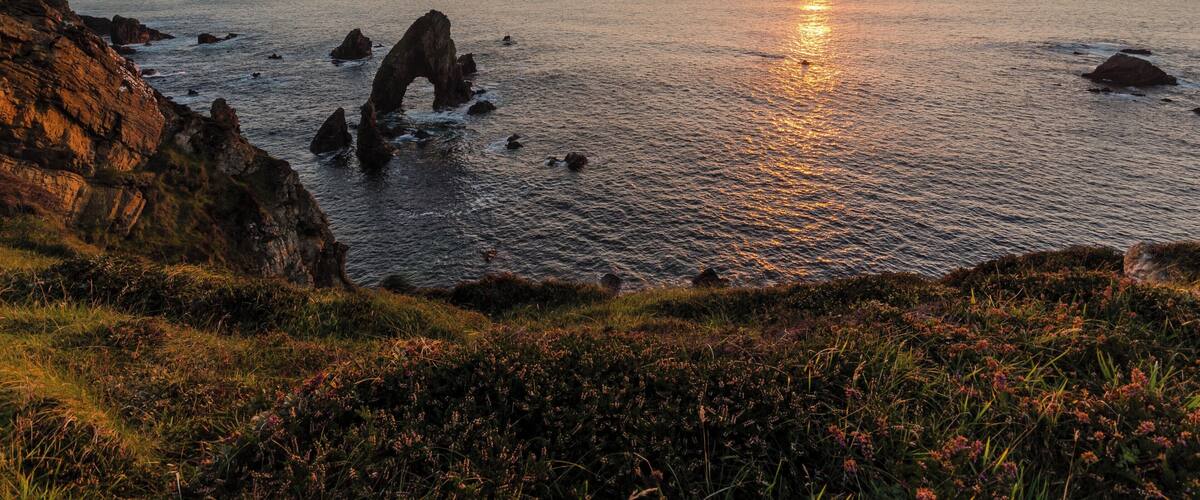 A coastal sunset with rocky formations and calm sea.