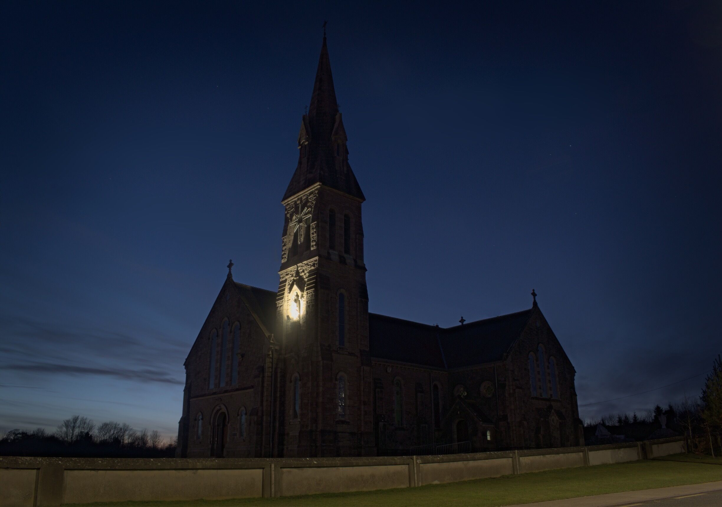 A large church with a tall steeple and a clock tower, surrounded by a grassy area.