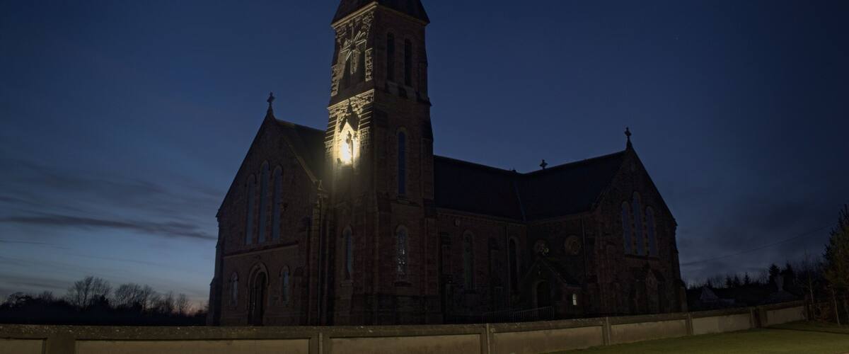 A large church with a tall steeple and a clock tower, surrounded by a grassy area.