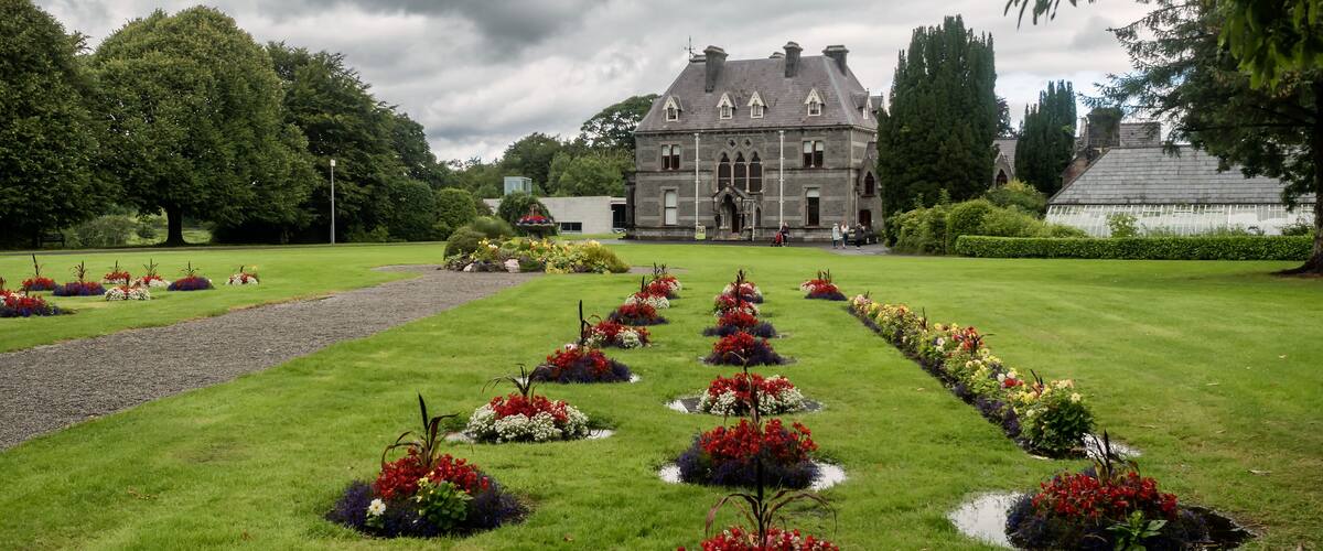 A large, historic building with a symmetrical garden featuring flower beds and a central pathway.