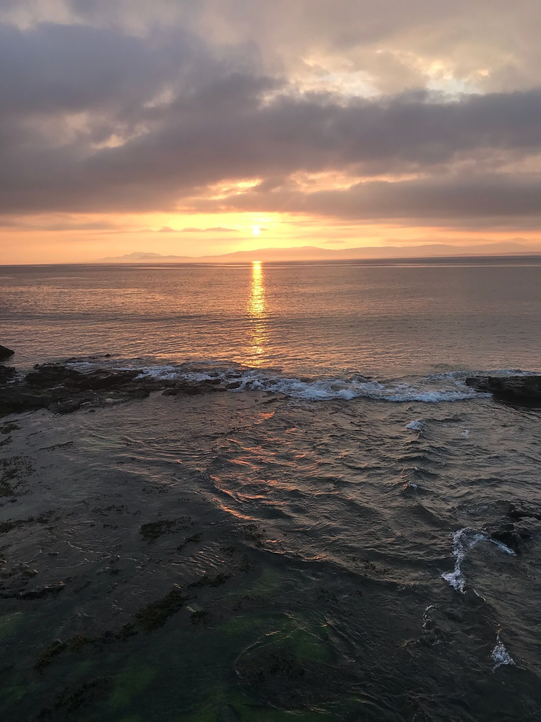 A sunset over a rocky coastline with waves crashing onto the shore.