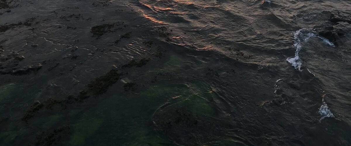 A sunset over a rocky coastline with waves crashing onto the shore.