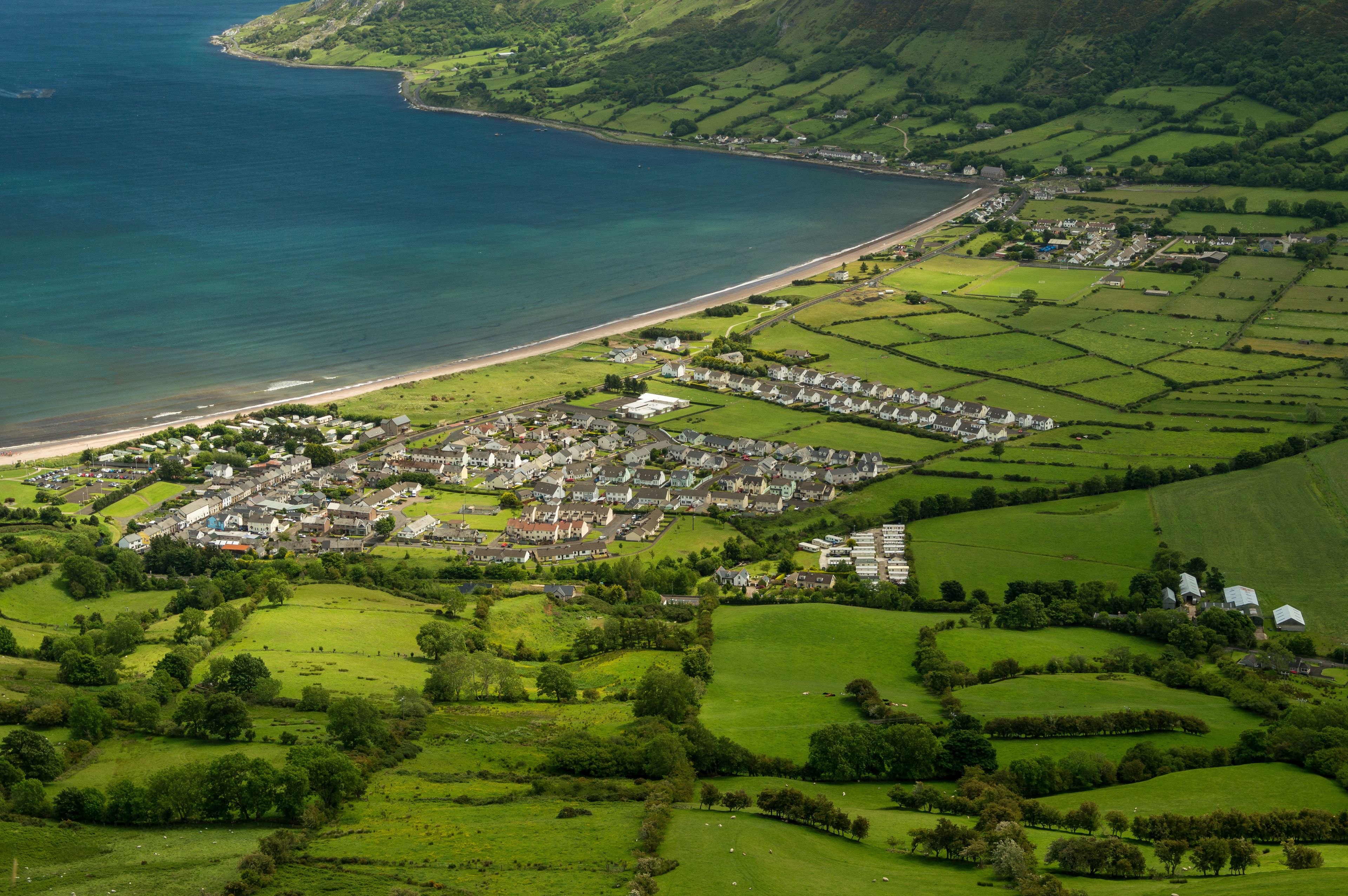 A coastal town with a beach, green fields, and a hilly landscape.