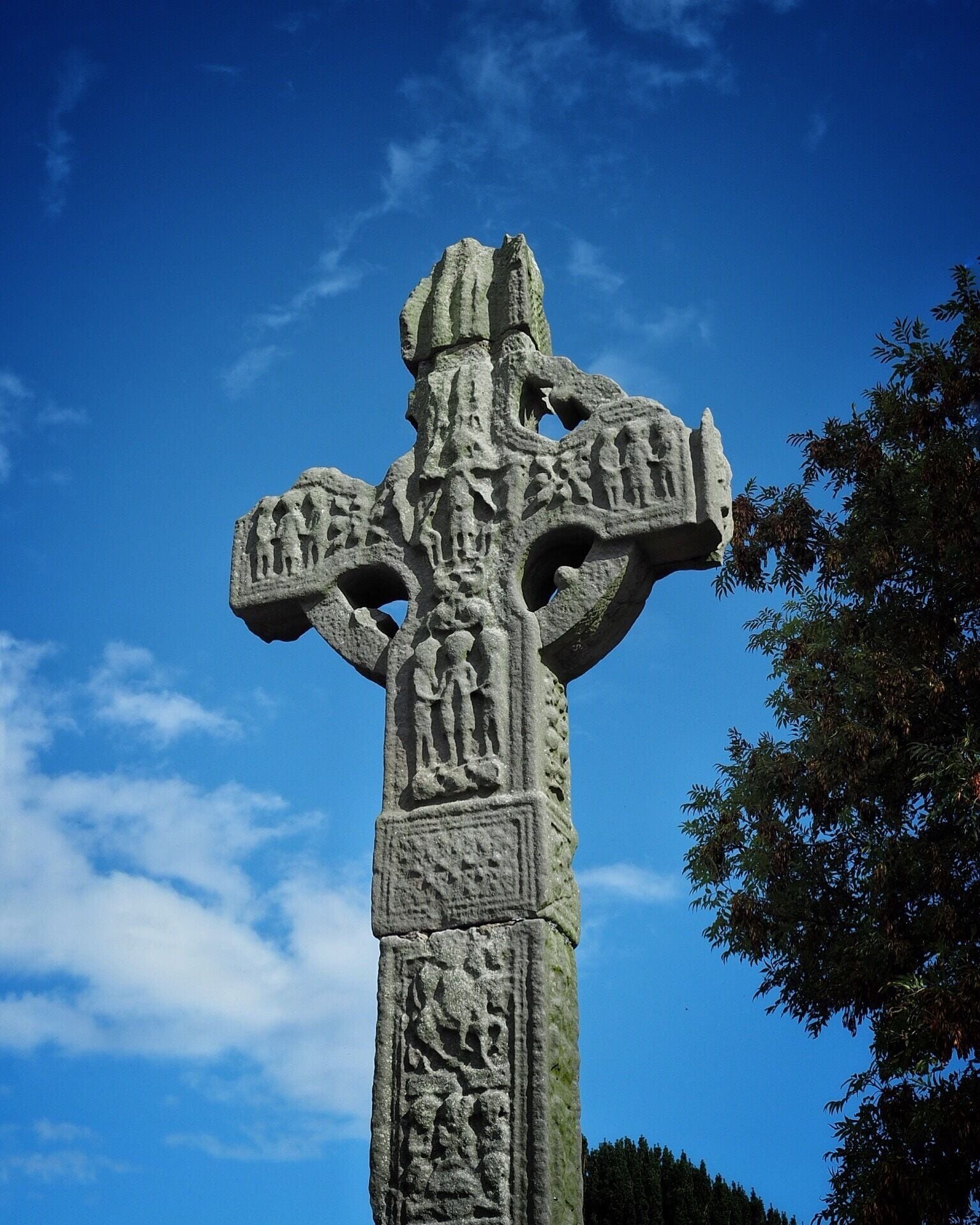 Ardboe High Cross (Irish: Seanchrois Ard Bó) is a high cross and national monument dating from the tenth century located in Ardboe, County Tyrone, Northern Ireland. The cross stands at the entrance to a cemetery and a monastery and a church from the seventeenth century which was founded in 590 by Saint Colman. The monastery was destroyed by fire in the twelfth century. It is believed to have been erected in either the ninth or the tenth century. The name "Ard Boe" means "hill of the cow" it comes from a legend that the monastery of Ardboe was built from the milk of a magic cow out of Lough Neagh and forms the only remaining part of an early monastery on the site. At around 18.5 feet (5.6 m), Ardboe High Cross is Northern Ireland's tallest cross. Although the head of the cross is damaged, it seems to be the only such cross in Northern Ireland to remain largely complete and original.