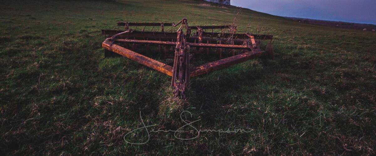 A grassy field with a rusty metal gate and a historic castle in the background.
