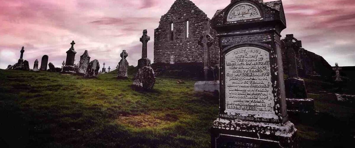 A cemetery with ancient stone crosses and a ruined church in the background.