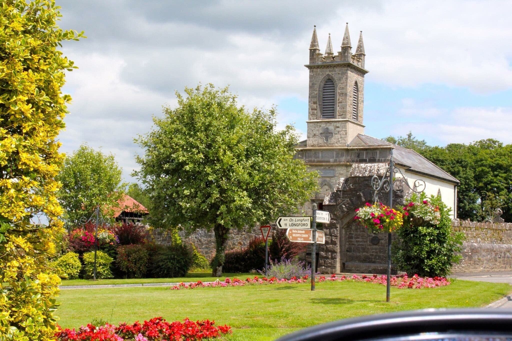 A church with a tall tower, surrounded by colorful flowers and greenery.