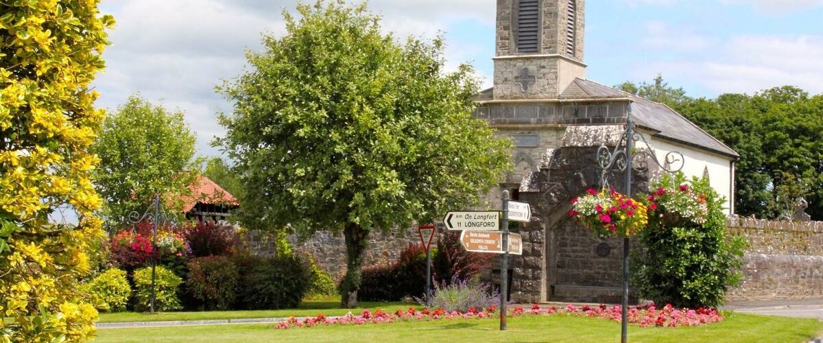 A church with a tall tower, surrounded by colorful flowers and greenery.