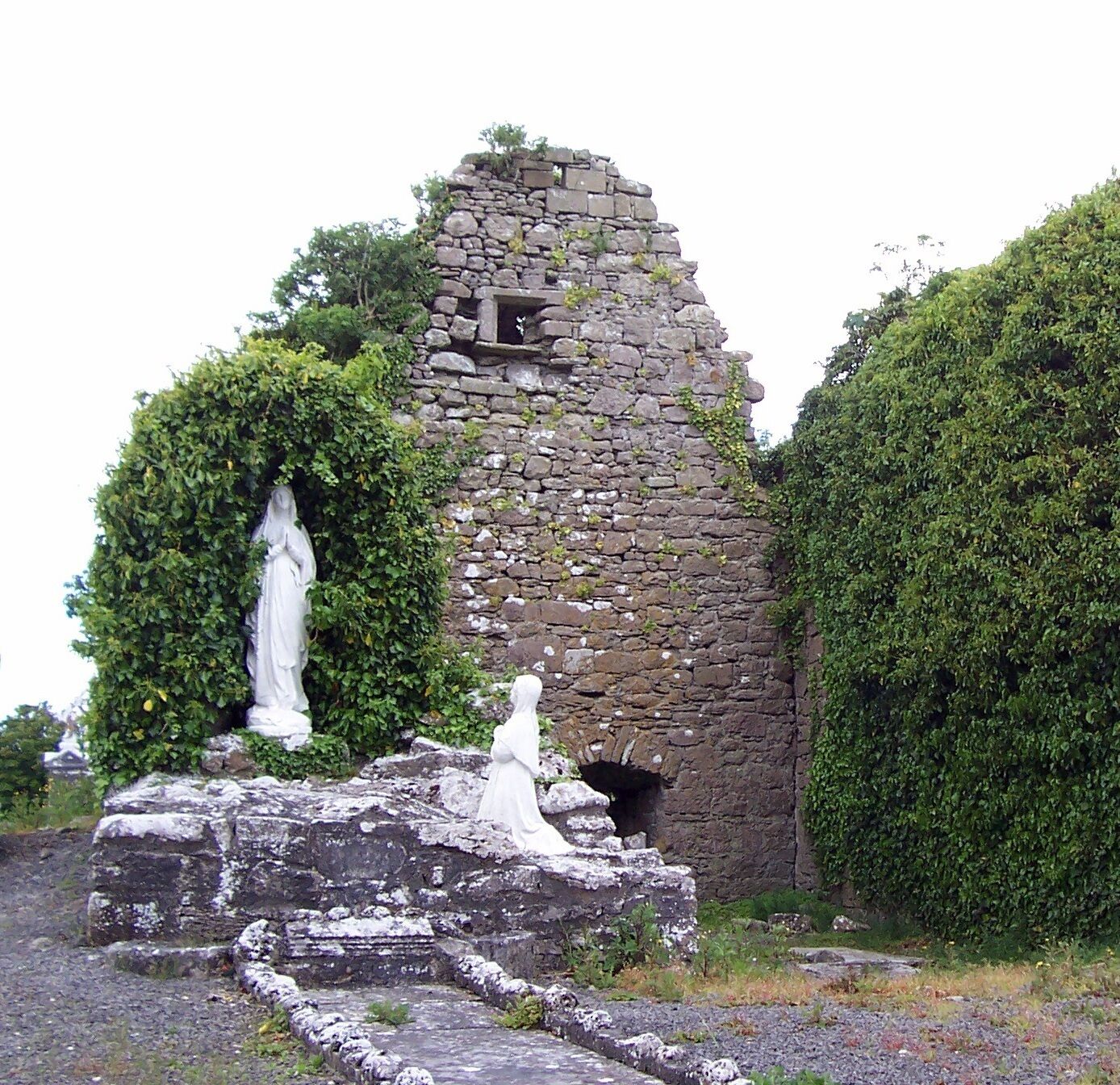 A stone ruin with a statue, surrounded by greenery.