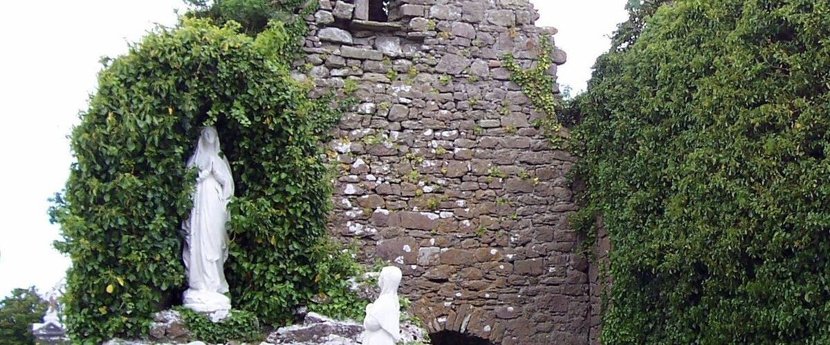 A stone ruin with a statue, surrounded by greenery.