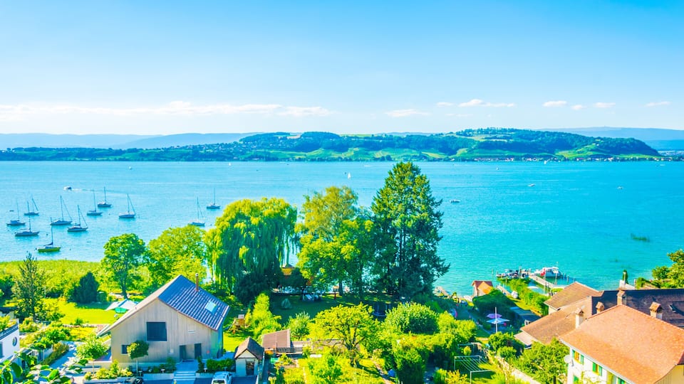 A lakeside village with boats, houses, and lush greenery.