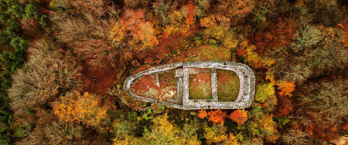 An aerial view of a circular stone structure surrounded by autumn-colored trees.