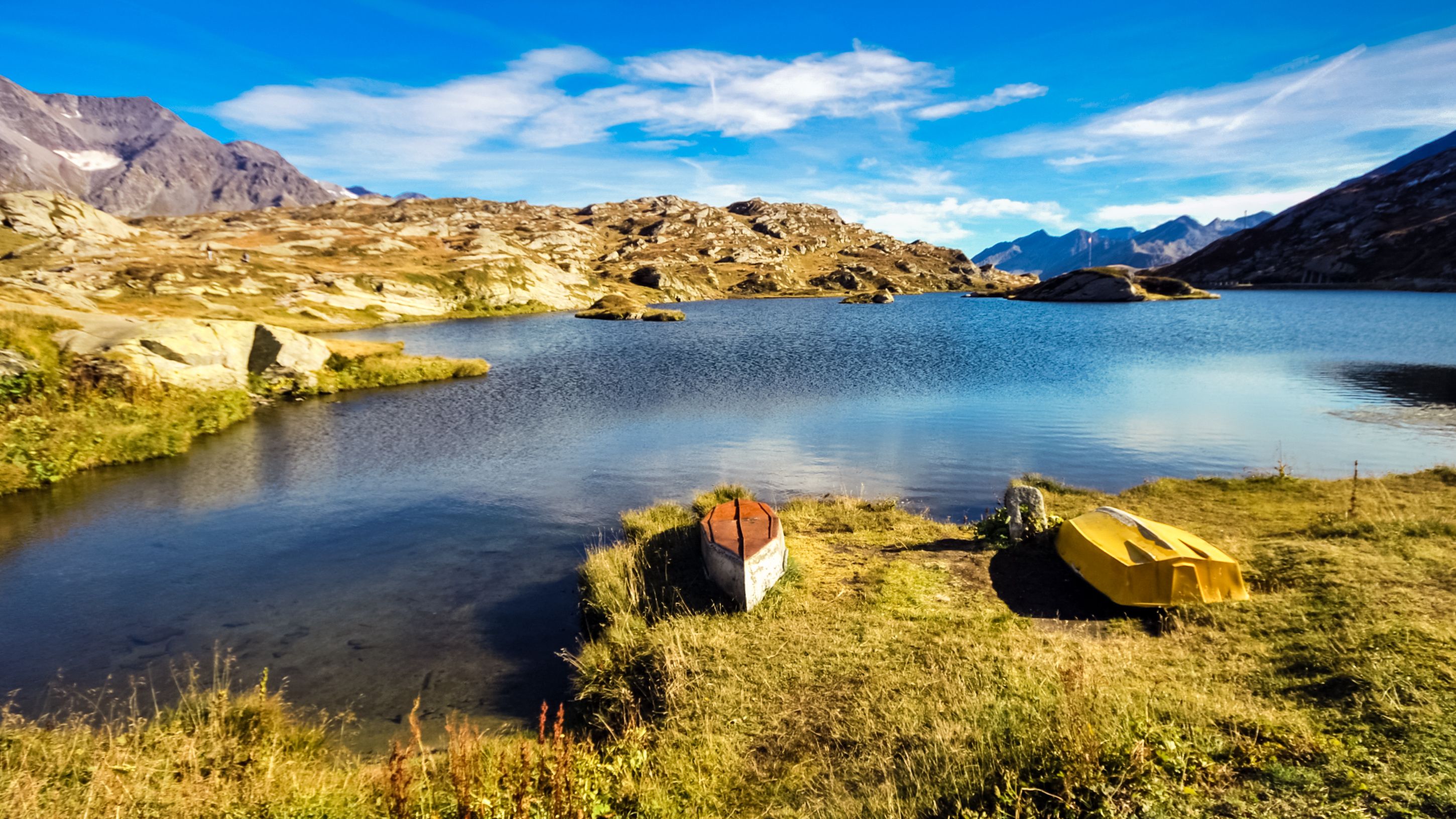 A calm lake surrounded by mountains, with two boats on the shore.