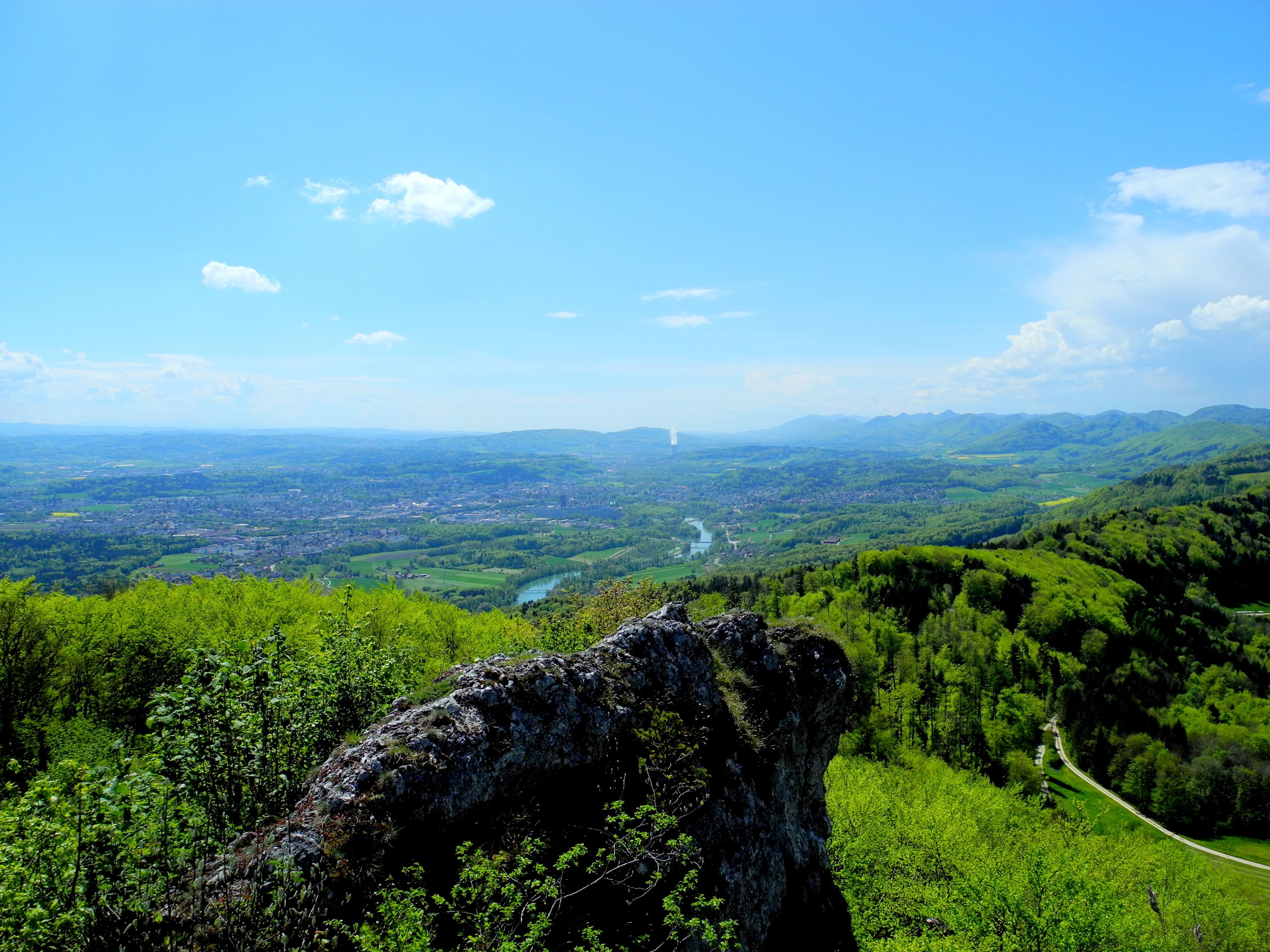 A mountainous landscape with a winding road, lush greenery, and a distant tower.
