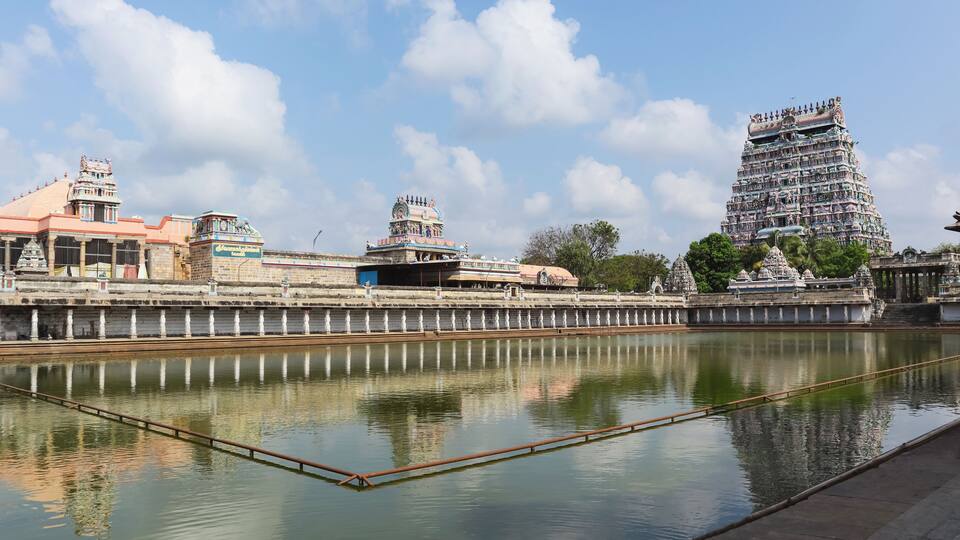 A temple complex with a large, multi-tiered tower and a calm river in the foreground.
